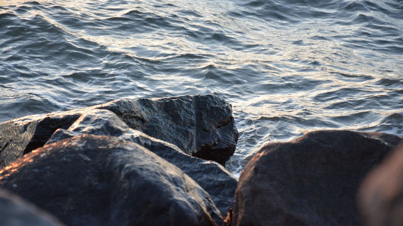 A lone rock standing firm as ocean waves crash at sunrise